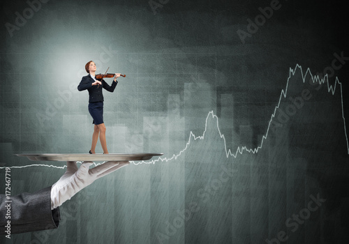 Attractive businesswoman on metal tray playing violin and graphs at background