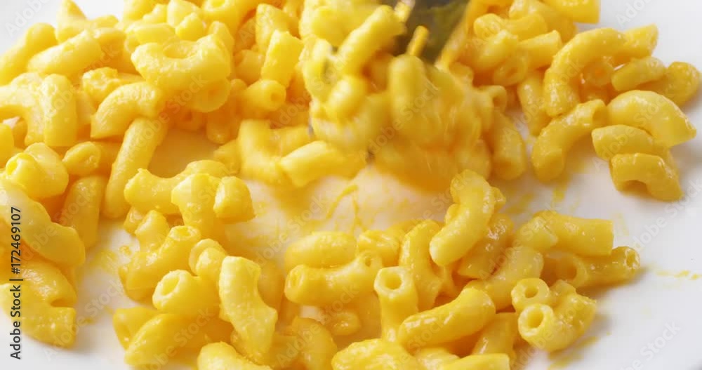 Close video of macaroni and cheese on a white plate being quickly mixed with a fork. Close video of macaroni and cheese on a white plate being quickly mixed with a fork.