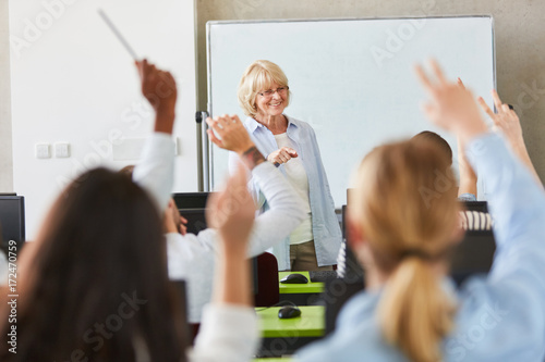 Viele Schüler im Unterricht heben die Hände photo