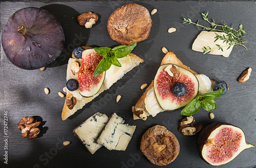 Overhead of figs, dried figs, snack sandviches with brie, blue cheese, fig slices, pine nuts and blueberry on black slate background. Top view. photo
