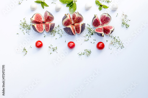 Overhead of food composition with figs, tomatoes cherry, mozzarella and sprouted alfalfa on white. Top view
