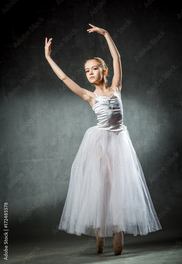 Fototapeta premium Beautiful young ballerina is dancing in the studio on a dark background. A little dancer. Ballet dancer.