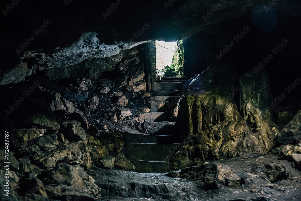 Dark cave with steps of staircase and light from entrance