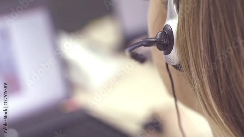 The operator of the hotline with headsets, sit at the computer in the office and advise clients. Workers call-center, a woman talking to customers. She prints on the computer and answers questions.
