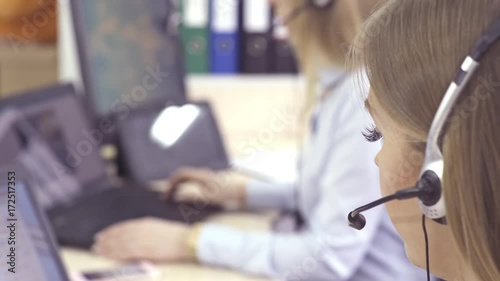 The operator of the hotline with headsets, sit at the computer in the office and advise clients. Workers call-center, a woman talking to customers. She prints on the computer and answers questions.