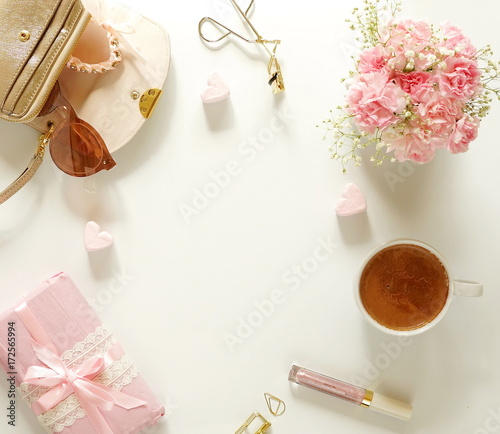 Feminine desk with bouquet of pink carnations in a vase, cup of cocoa , accessories, gift in pink packing and pink hearts on a white background. Holiday concept. Top view. copy space