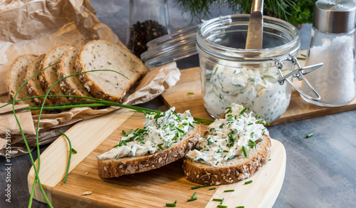Billede på lærred Home made bread on a wooden cutting board with curd cheese and ricotta and herbs