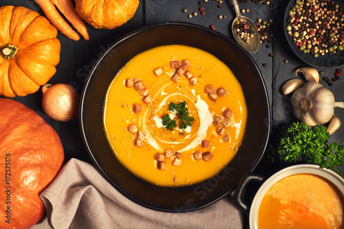Pumpkin creme soup in a dark crockery served with croutons, crushed nuts and cream