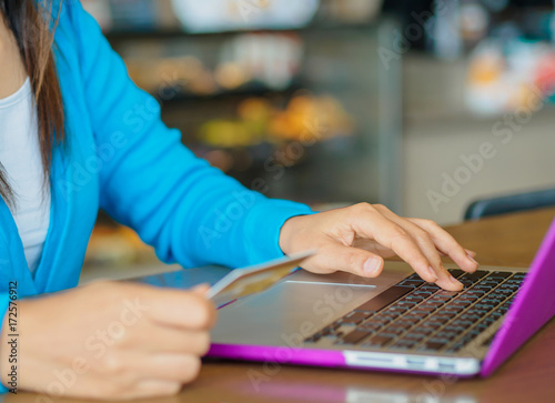 Pretty Young woman hands holding a credit card and using laptop computer for online payment in a cafe.