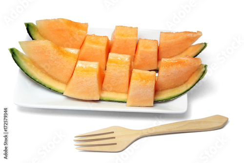 Sliced orange melon in pieces on a white plate with wooden fork on white background.