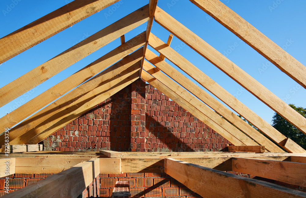 Fototapeta premium Wooden roof construction. Unfinished House building. Installation of wooden beams at construction the roof truss system of the house.