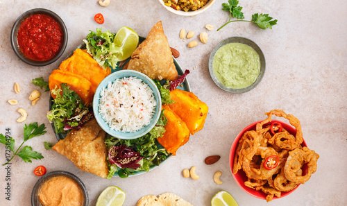 Assorted Indian snacks with rice, salad and sauces on rustic surface. Top view, blank space