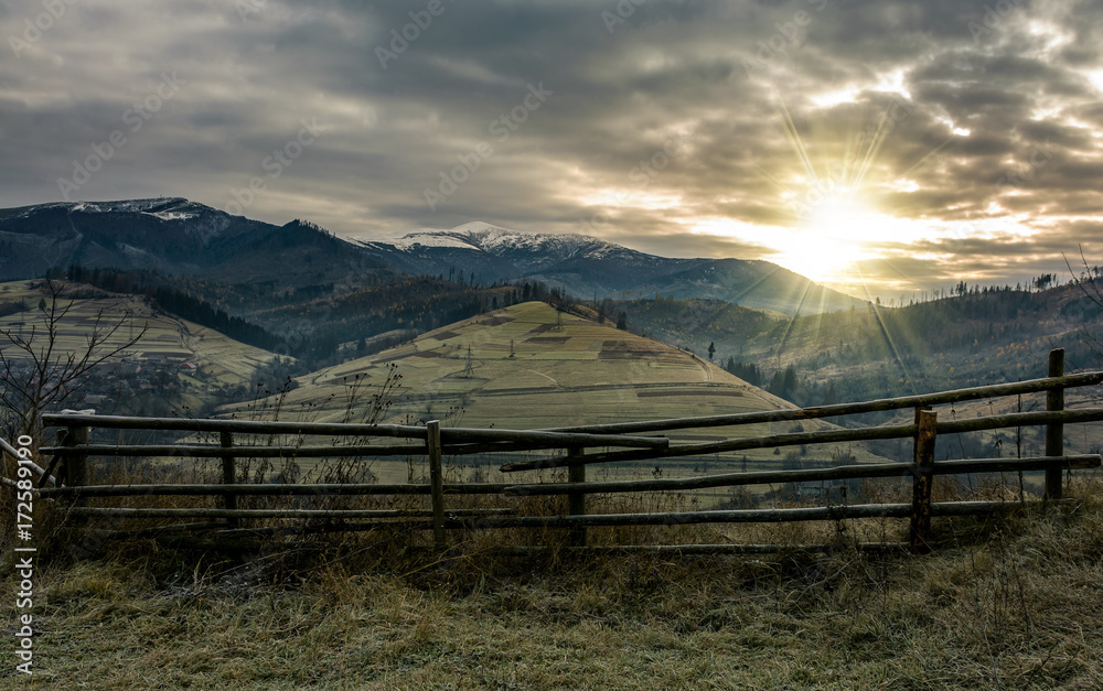 fence on hillside in late autumn gloomy sunrise. high mountain ridge with snowy tops in a distance under overcast sky