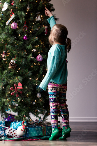A young girl with is decorating a Christmas tree and is happily playing with the decorations.