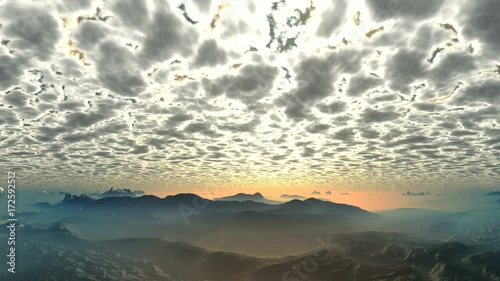 Sunset under the Luminous Clouds. Dense and low, luminous clouds are floating in the sky. In the lowlands between the hills lies a dense orange mist. Horizon lit by the sunset. 