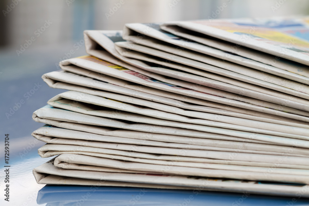 Time to read concept. Newspapers folded and stacked on the blue surface and blur background. Closeup, selective focus Time to read concept. Newspapers folded and stacked on the blue surface and blur background. Closeup, selective focus