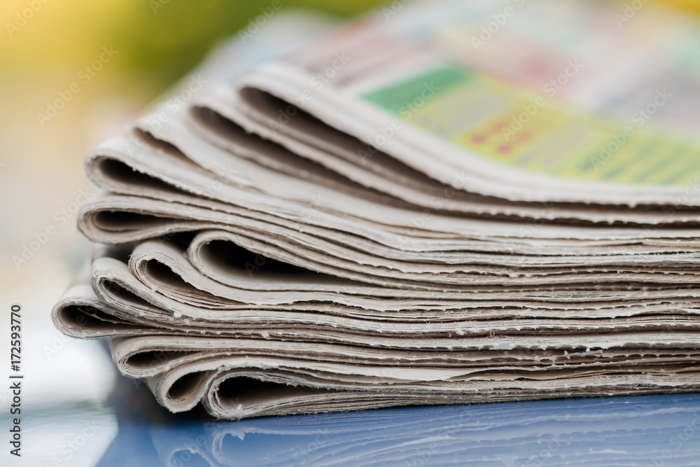 Time to read concept. Newspapers folded and stacked on the blue surface and blur background. Closeup, selective focus Time to read concept. Newspapers folded and stacked on the blue surface and blur background. Closeup, selective focus