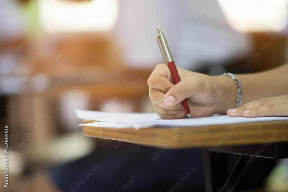 Closeup to hand of student  holding pen and taking exam in classroom with stress for education test . - obrazy, fototapety, plakaty 