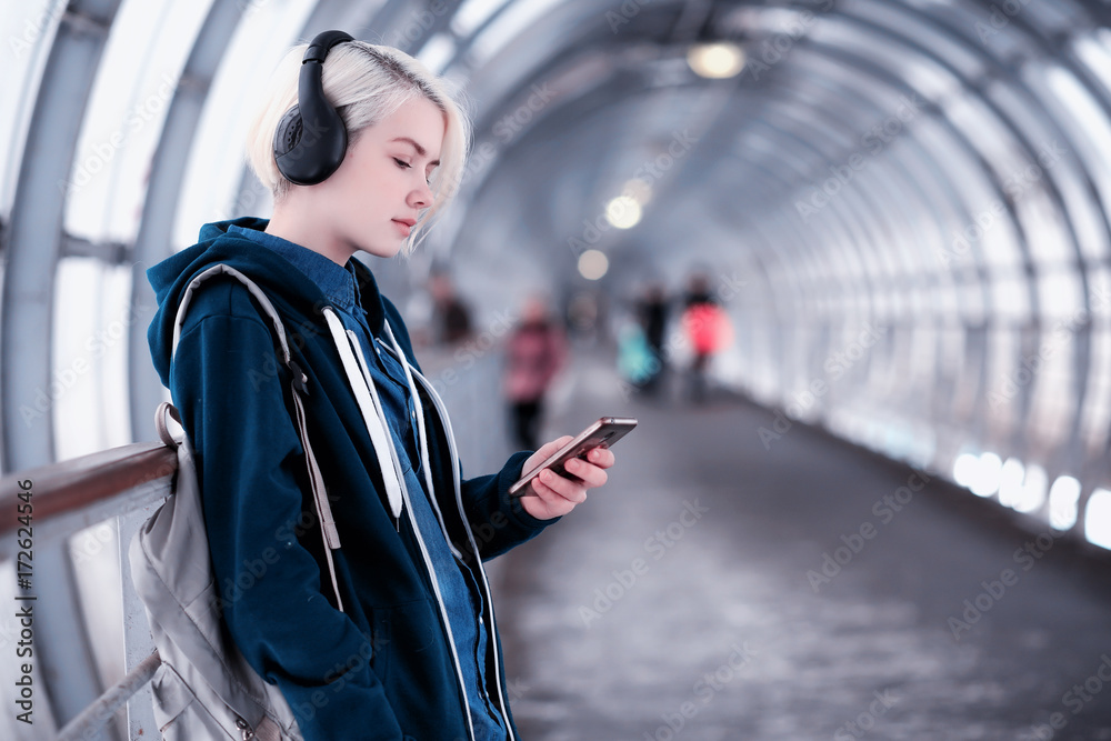 Young student listening to music in big headphones in the subway tunnel