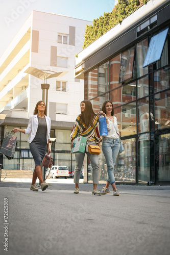 Three fashionable young women strolling with shopping bags. Women walking on street.