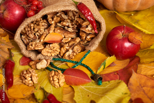 Nuts in a sack, fruits and vegetables on fallen leaves background, autumn season