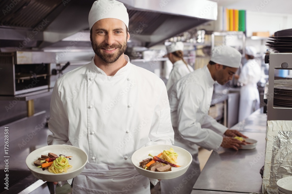 Smiling chef holding delicious dish in kitchen Smiling chef holding delicious dish in kitchen