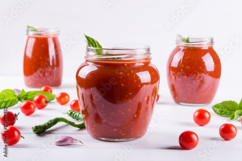 Tomato sauce, ketchup in glass jar and ingredients on a white background 