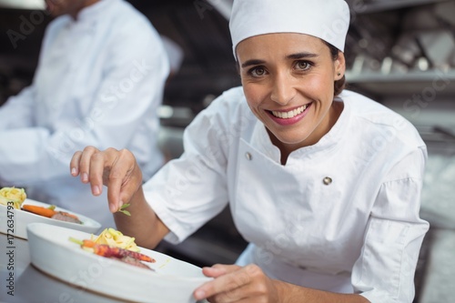 Female chef garnishing food in kitchen at restaurant photo