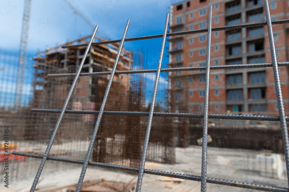 Reinforcement net of concrete in the construction site, metal rods for strength with a building under construction on the background