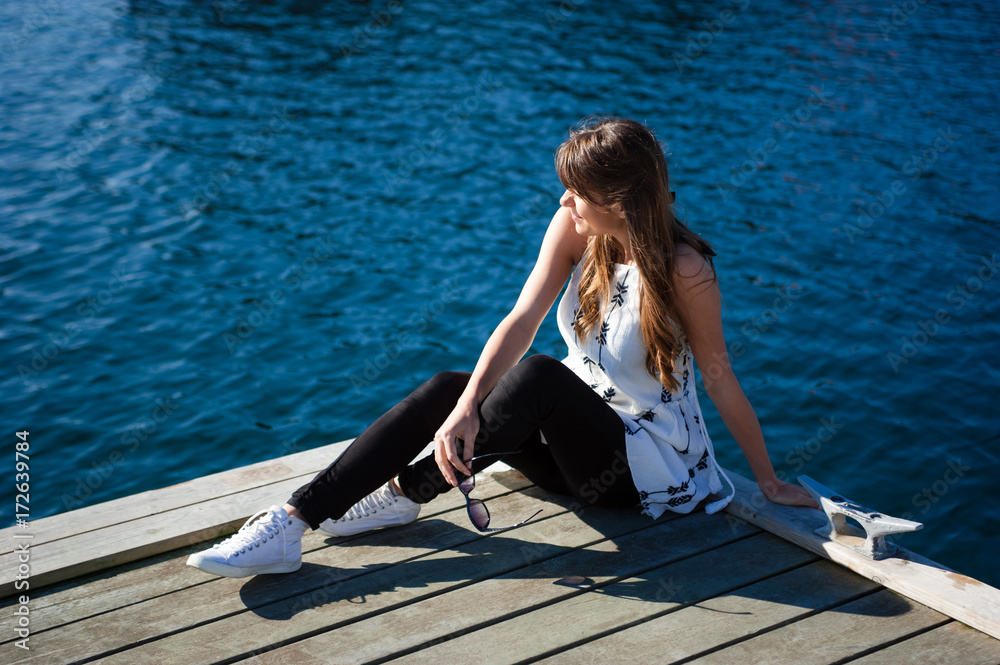 Young and happy tourist woman sitting in the harbor on wood pier Young and happy tourist woman sitting in the harbor on wood pier