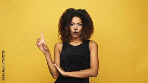 Young displeased african woman with cat make-up and ears showing NO gesture isolated over yellow
 photo