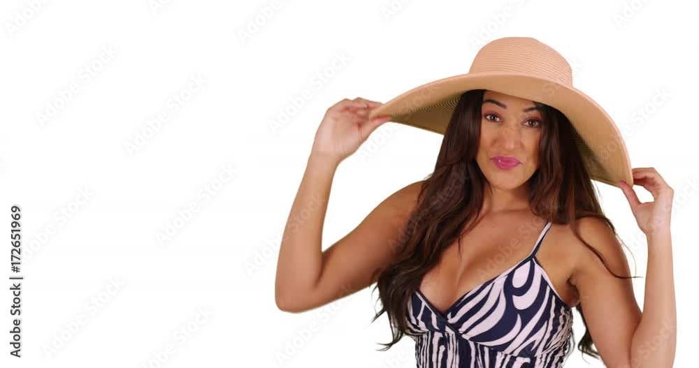 Cheerful Latina female modeling floppy sunhat on white background, laughing and smiling. Happy carefree tourist posing in sundress in studio. 4k Cheerful Latina female modeling floppy sunhat on white background, laughing and smiling. Happy carefree tourist posing in sundress in studio. 4k