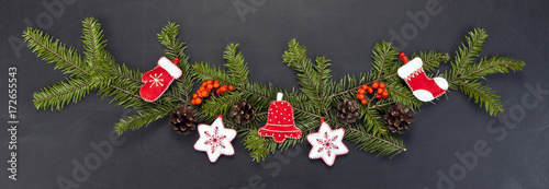 Christmas floral decoration with toys, holly berry, pine cones and winter greenery over chalkboard.