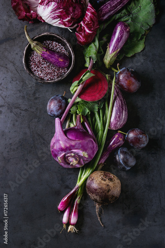 Assortment raw organic of purple vegetables mini eggplants, spring onion, beetroot, radicchio salad, plums, kohlrabi, flower salt over dark metal background. Top view with space