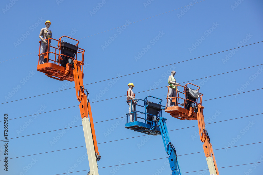 Hydraulic mobile construction platform elevated towards a blue sky with false construction workers . dummy man