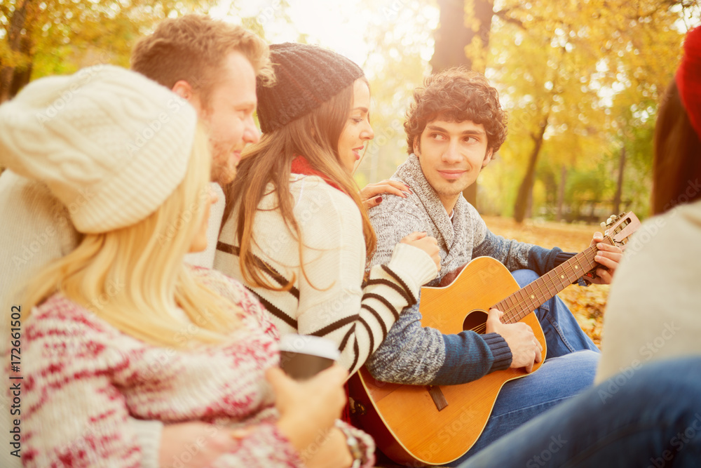     Friends having a good time in park at autumn/ singing and playing guitar 