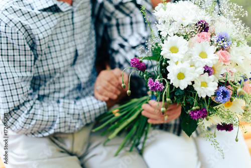 two old people are sitting on a bench and holding each other's hands against a beautiful bouquet of flowers