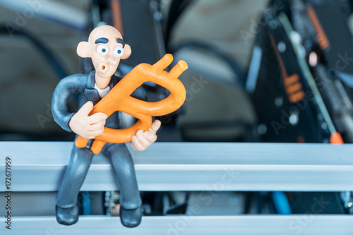 Bald plasticine businessman sits on a mining farm with bitcoin in his hand