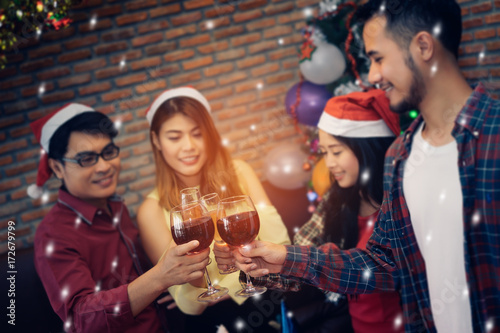 Young men and women asian group together clink glasses drinking wine or champagne in chrismas party new year celebrate with snow effect at home