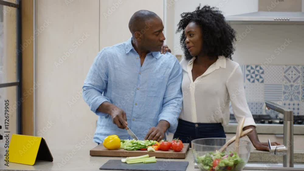 Happy affectionate couple dancing while they prepare a meal together in the kitchen at home.