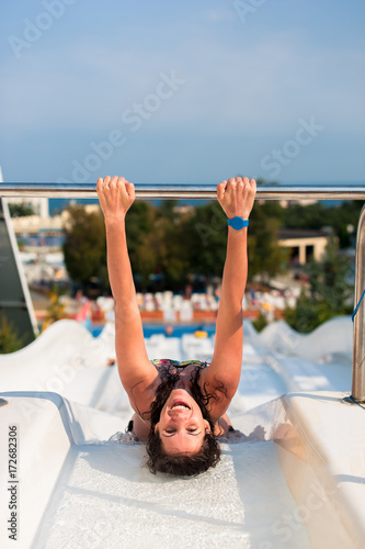 Happy young woman in a water fun park on top of water slide looking at camera, having a good time on a summer hot day.