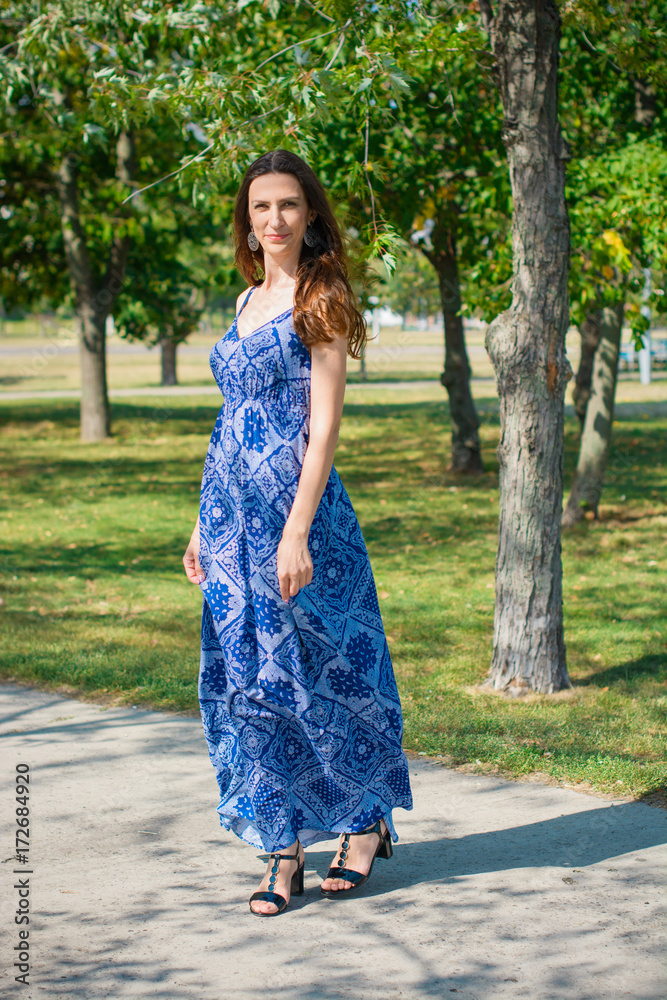 A middle-aged woman is stylishly dressed in a long blue dress, resting near the city park, enjoying the day A middle-aged woman is stylishly dressed in a long blue dress, resting near the city park, enjoying the day