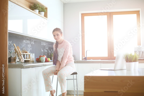 Young woman sitting on table in the kitchen.