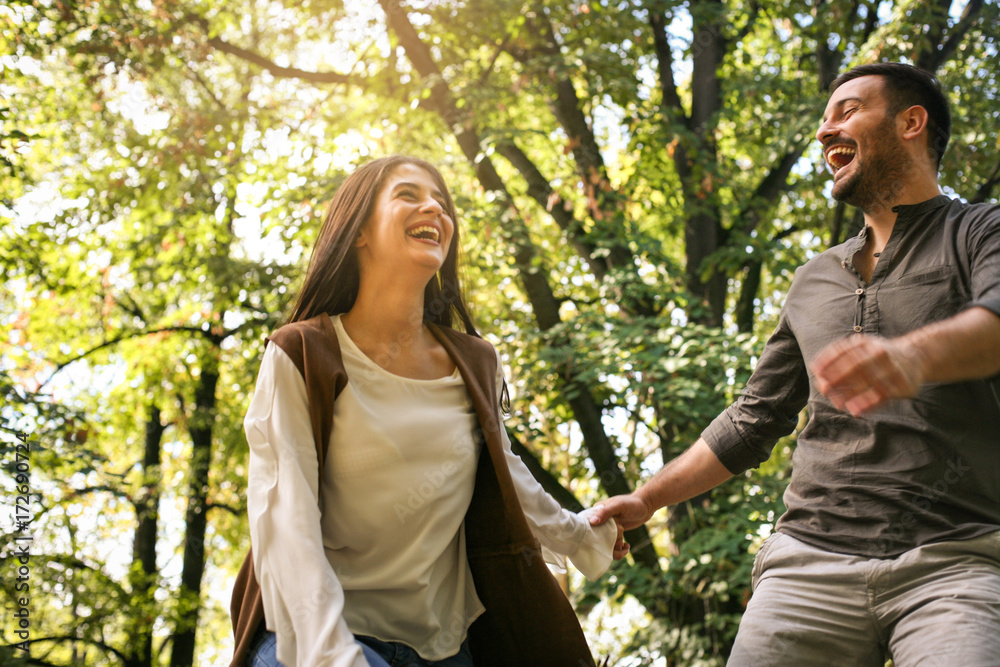 Young couple holding hands and running together trough park.