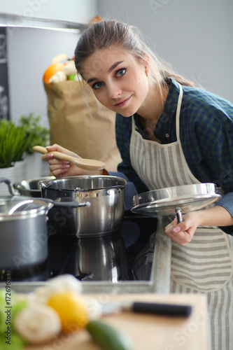 Young woman standing by the stove in the kitchen .