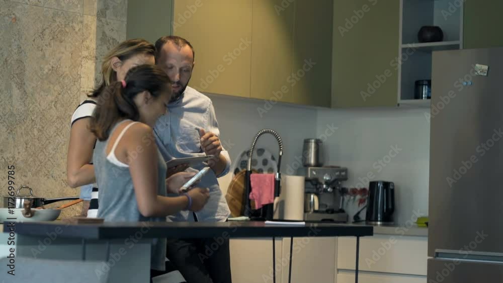 Family talking, using smartphone and tablet in kitchen
