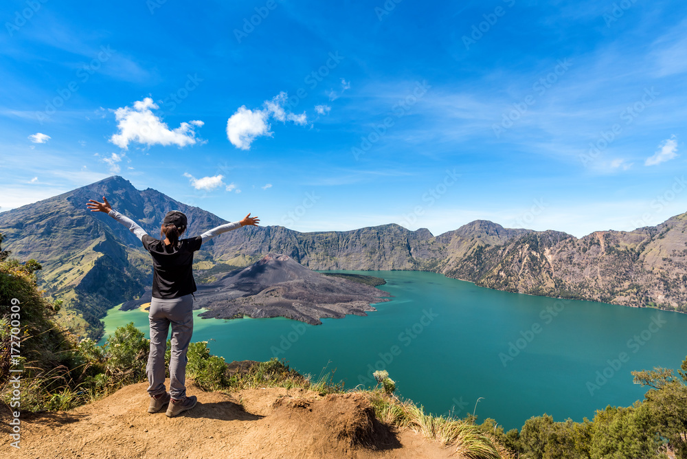 Woman spreading hand, enjoy and happy with active volcano Baru Jari, Lake Segara Anak and summit of Rinjani mountain view after finished climbing at Rinjani mountain, Lombok, Indonesia.