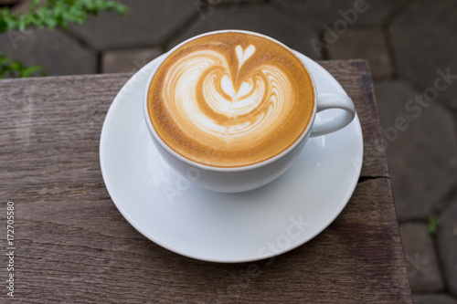 A white cup of coffee latte art on wood table