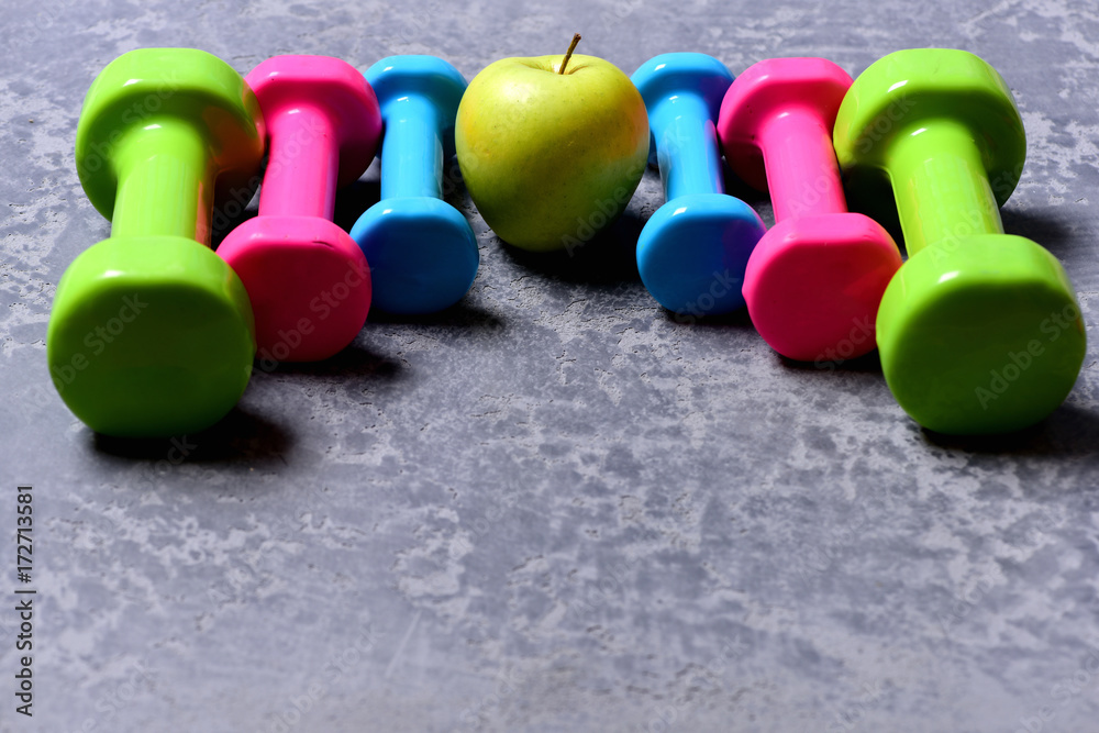 Barbells in different colors and apple placed in pattern, closeup Barbells in different colors and apple placed in pattern, closeup
