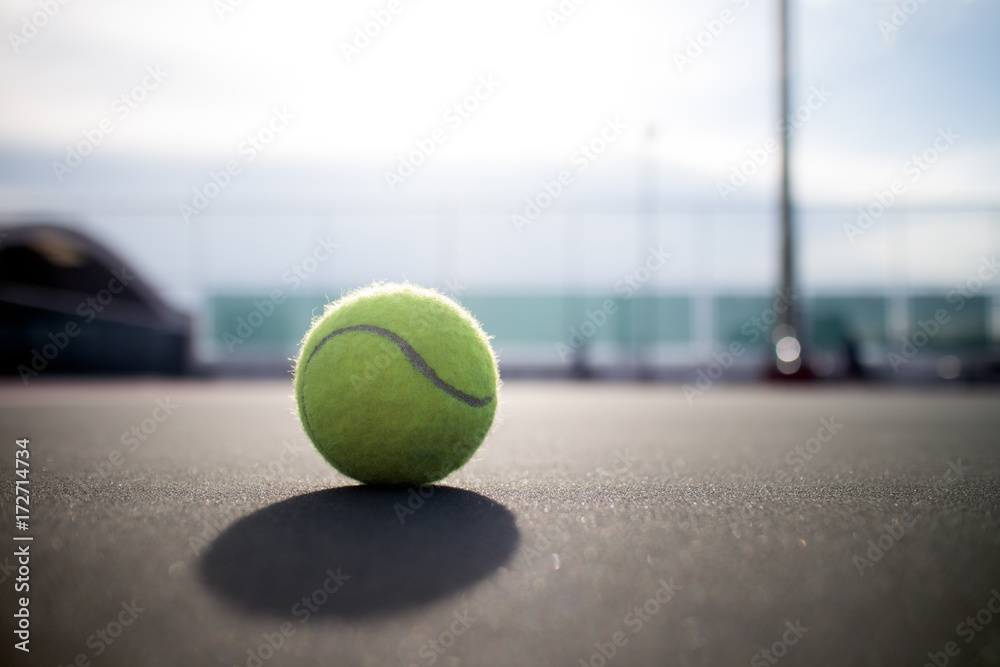 Tennis ball on hard court under sunlight